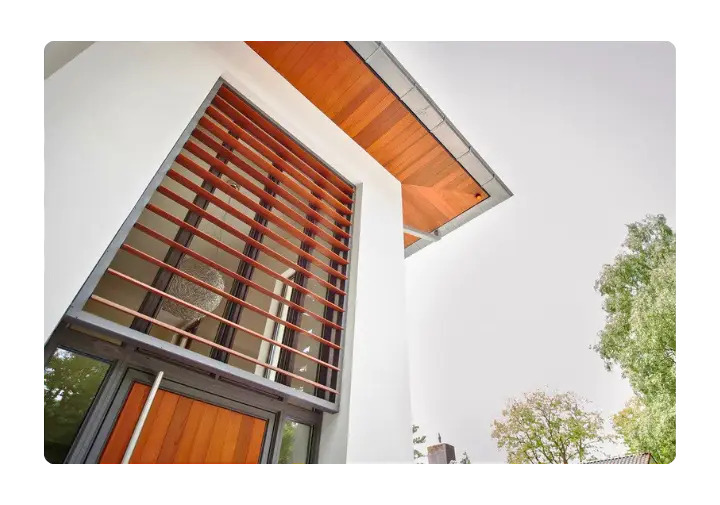 Upward view of a modern building featuring a large window with horizontal timber sun louvres.