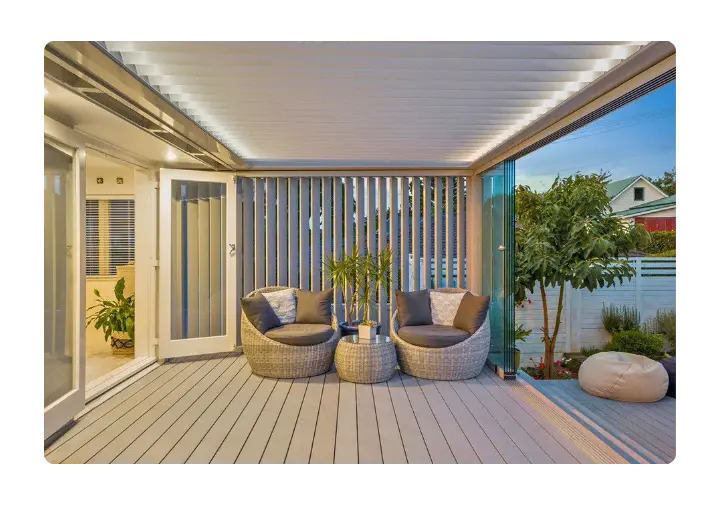 Outdoor patio with a retractable louvered roof, two wicker chairs, and vertical slat screens.