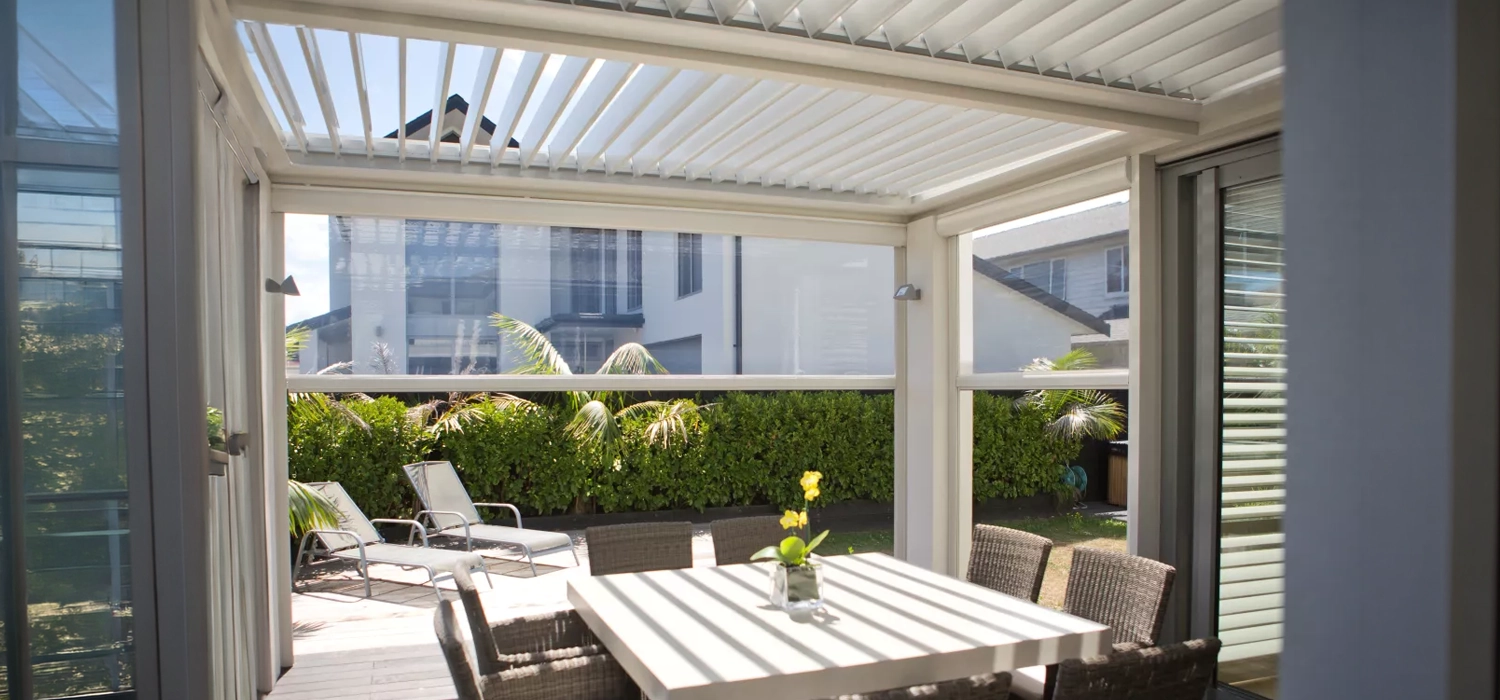 A patio featuring a table and chairs, sheltered by a roof and equipped with mesh outdoor blinds for privacy and shade.