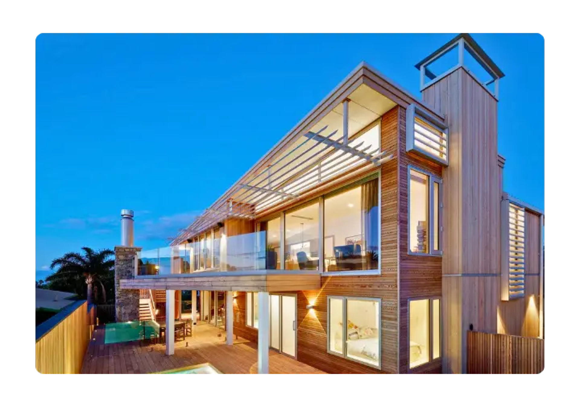 Modern multi-story home with wooden siding, large windows, and sun louvres at dusk.