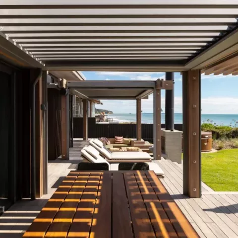Outdoor living area with a Louvretec opening roof overlooking the ocean and lawn.