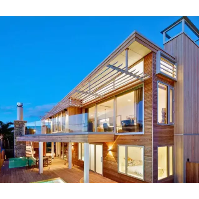 Modern multi-story home with wooden siding, large windows, and sun louvres at dusk.