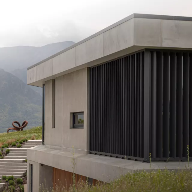 Modern concrete home with vertical sun louvre screens from the Sun Louvre Collections, providing privacy and shading with a mountain backdrop